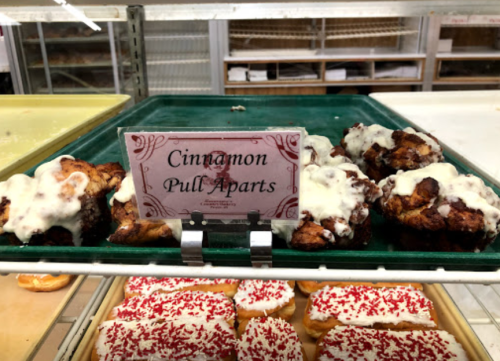 A display of cinnamon pull-apart pastries topped with white icing, labeled on a sign in a bakery.
