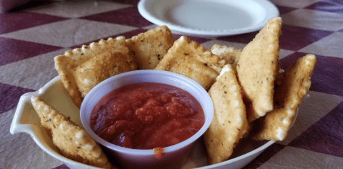 A bowl of crispy, seasoned crackers served with a side of red salsa on a checkered tablecloth.
