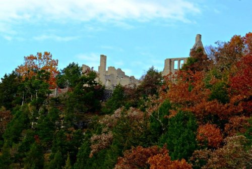 Ruins of a stone structure atop a hill, surrounded by vibrant autumn foliage and a clear blue sky.