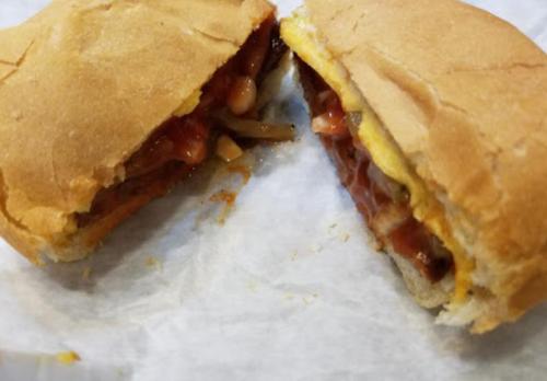 A sandwich cut in half, filled with meat, cheese, and sauce, resting on white paper.