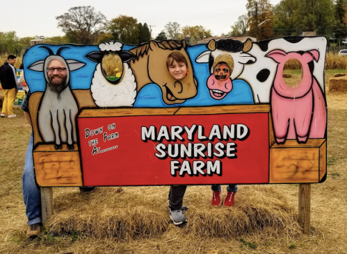 A farm-themed cutout board with a man and a girl posing as animals, featuring a sign that reads "Maryland Sunrise Farm."