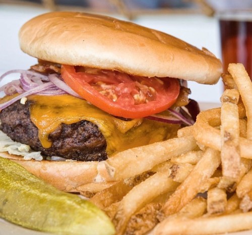 A juicy cheeseburger with bacon, lettuce, tomato, and onions, served with crispy fries and a pickle on the side.