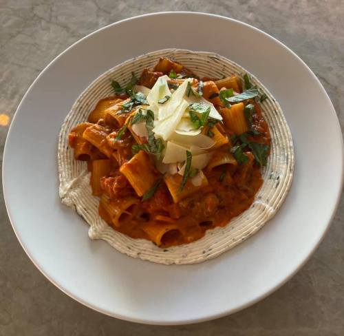 A plate of rigatoni pasta in a creamy sauce, garnished with herbs and cheese, served on a circular white dish.