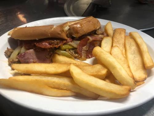 A plate with a sandwich filled with meats and vegetables, accompanied by golden French fries.