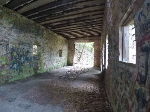 Interior of a dilapidated stone building with graffiti on the walls and a view of nature through an open doorway.