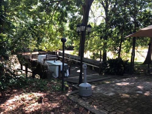 A serene outdoor setting featuring a wooden bridge, tables, and lush greenery under dappled sunlight.