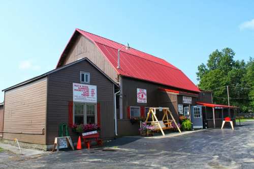 A rustic barn with a red roof, featuring signs and flower boxes, set against a clear blue sky.