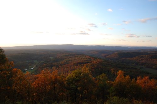 A scenic view of rolling hills covered in autumn foliage under a clear sky, with a river winding through the landscape.