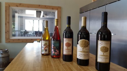 Five bottles of Spenker Winery wine on a wooden table, with a modern tasting room visible in the background.