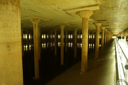 A dimly lit underground space with tall columns reflecting in still water.