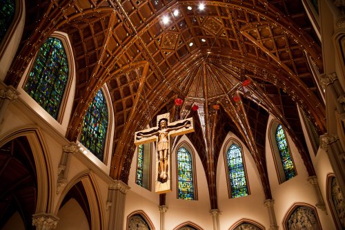 A grand church interior featuring a wooden crucifix and intricate stained glass windows under a vaulted ceiling.