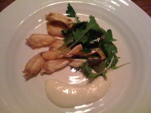 A plate featuring cooked frog legs, garnished with fresh greens and a creamy sauce on the side.