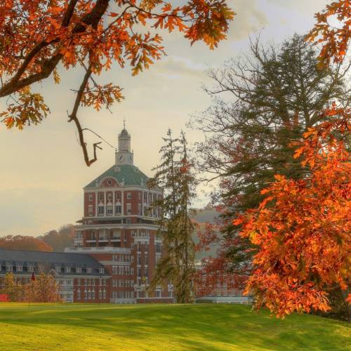 A scenic view of a historic building surrounded by vibrant autumn foliage and a clear sky.