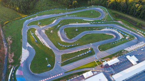 Aerial view of a go-kart track with winding paths, surrounded by green grass and trees.