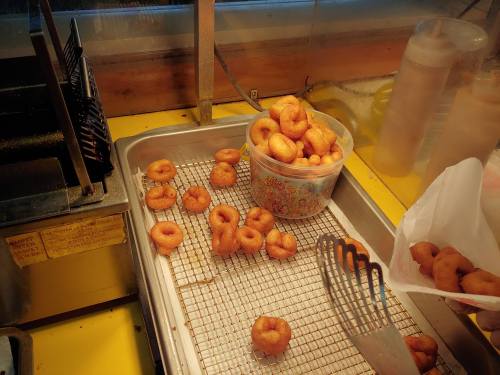 A tray with freshly fried mini donuts, some in a container, and a spatula nearby on a yellow countertop.