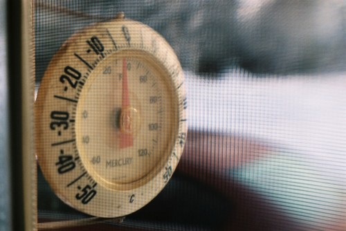 A close-up of a vintage mercury thermometer showing a temperature reading against a mesh background.