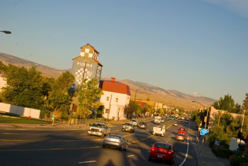 A scenic view of a road with cars, featuring a tall building with a Purina sign and mountains in the background.