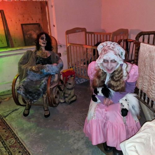 A creepy scene featuring a lifelike doll in a rocking chair and a girl in a pink dress holding small animals, both in a dimly lit room.