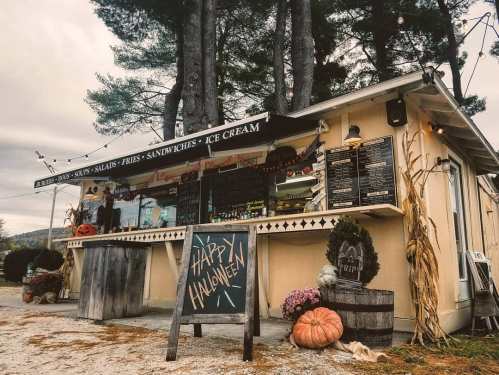 A cozy food stand decorated for Halloween, featuring a chalkboard sign, pumpkins, and autumn decor.