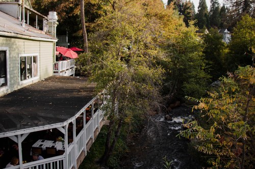 A riverside view of a green building with a deck, surrounded by trees and autumn foliage.