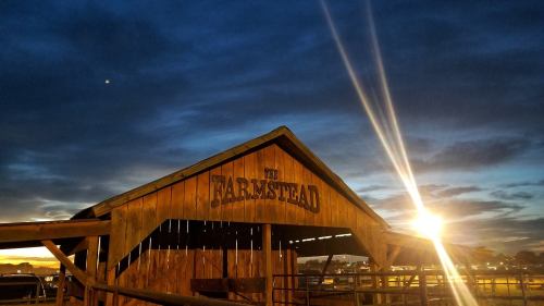 A rustic barn with "The Farmstead" sign, illuminated by a sunset, under a dramatic sky with clouds.