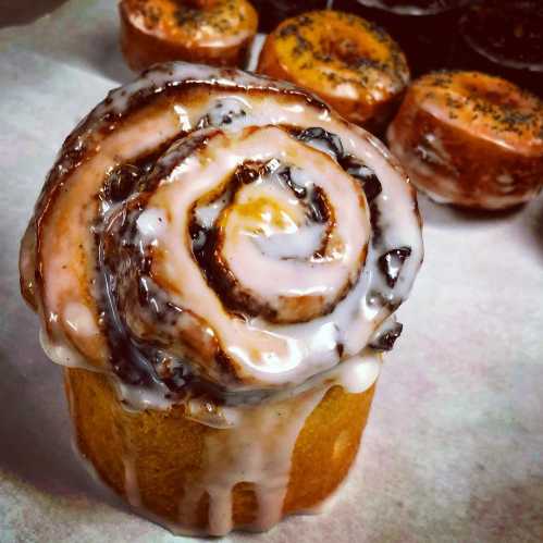 A close-up of a glazed cinnamon roll with a spiral design, sitting on a tray with other pastries in the background.