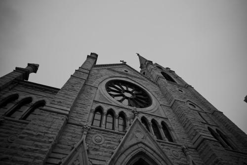 A low-angle view of a stone church with a large circular window and a tall steeple against a gray sky.