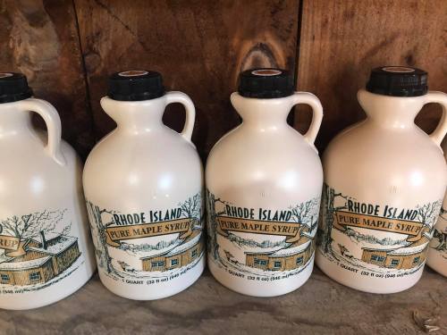 Four white jugs of Rhode Island pure maple syrup lined up on a wooden surface.