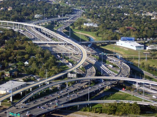 Aerial view of a busy highway interchange with multiple lanes and overpasses surrounded by greenery and buildings.