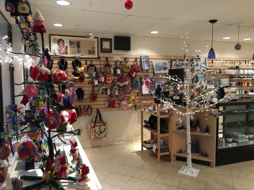 A cozy shop filled with colorful crafts, ornaments, and decorations, featuring a white tree and various handmade items.