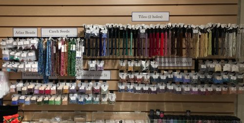 A display of various beads and tiles organized on a wall, labeled by type and size, showcasing colorful options.