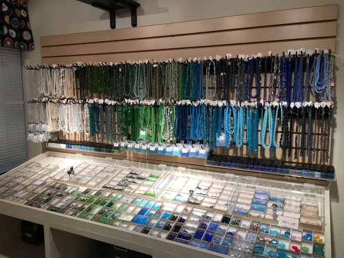A display of colorful beads and gemstones arranged on shelves and in trays, showcasing various shades of blue and green.