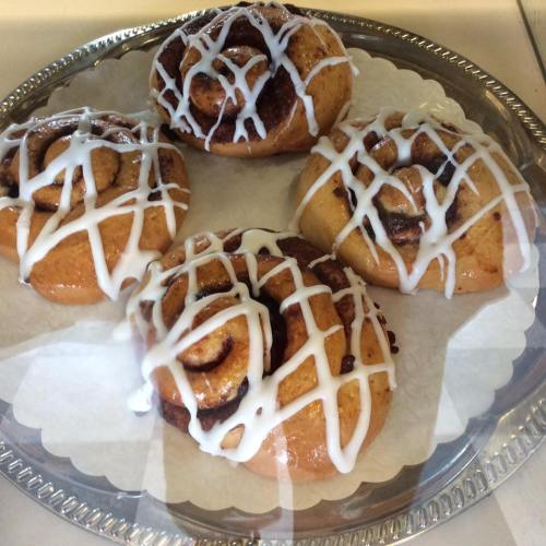 Four cinnamon rolls drizzled with white icing on a decorative silver platter.