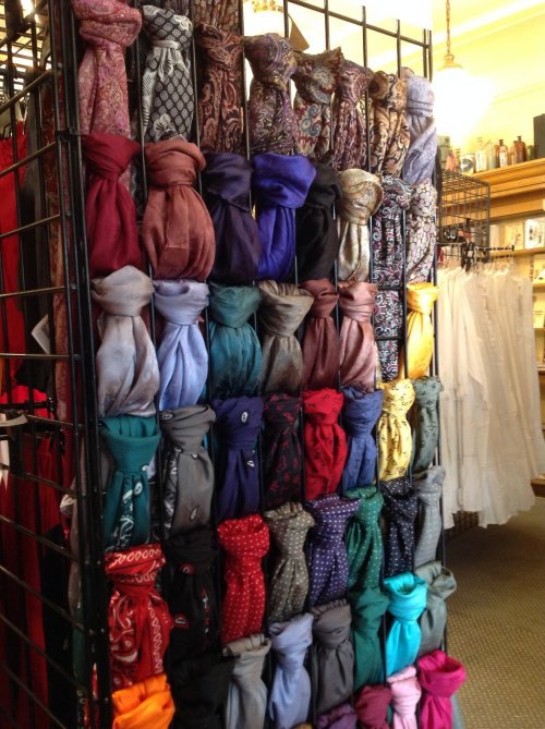 A display rack filled with various colorful scarves neatly tied and organized by color and pattern.
