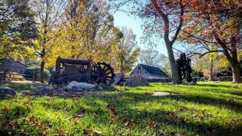 A rustic scene featuring an old tractor, stone path, and a barn surrounded by colorful autumn trees.