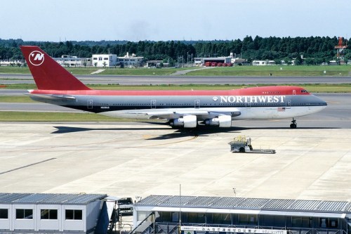 A Northwest Airlines Boeing 747 taxiing on an airport runway with a terminal in the foreground.