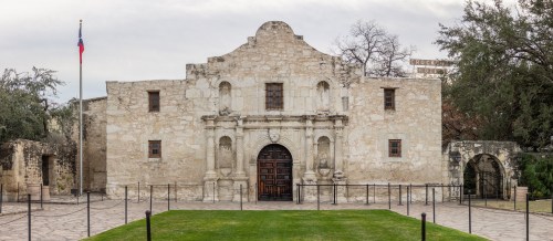 Historic Alamo building with stone facade, surrounded by a grassy area and a flagpole, under a cloudy sky.