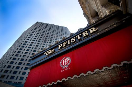 Sign of The Pfister Hotel with a red awning, featuring the establishment year 1893, against a city skyline backdrop.