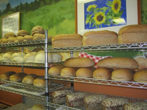 A display of various freshly baked breads on metal racks, with a colorful sunflower painting in the background.