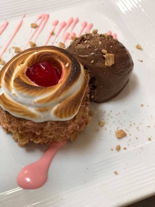 A dessert plate featuring a toasted meringue topped treat with a cherry and a scoop of chocolate ice cream.