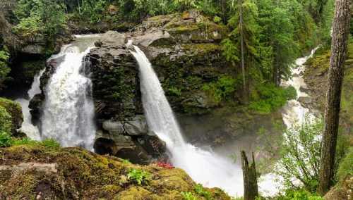 A scenic view of a waterfall cascading over rocky cliffs, surrounded by lush green trees and mist.