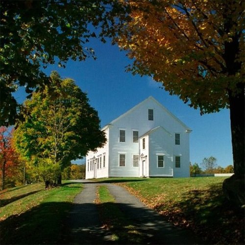A white house surrounded by colorful autumn trees under a clear blue sky.