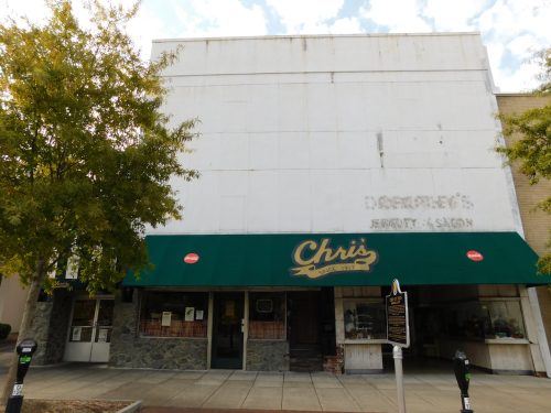 A storefront with a green awning reading "Chris" and faded signage above, surrounded by trees and a sidewalk.