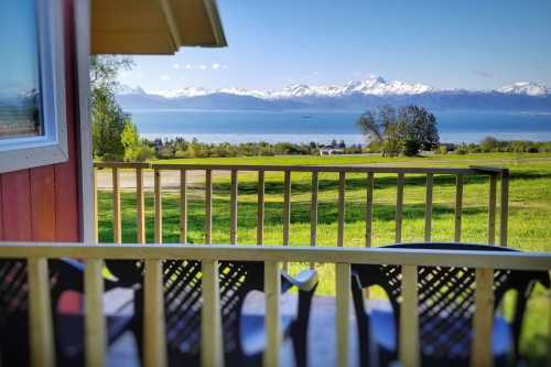 A scenic view from a porch overlooking a lake and snow-capped mountains under a clear blue sky.