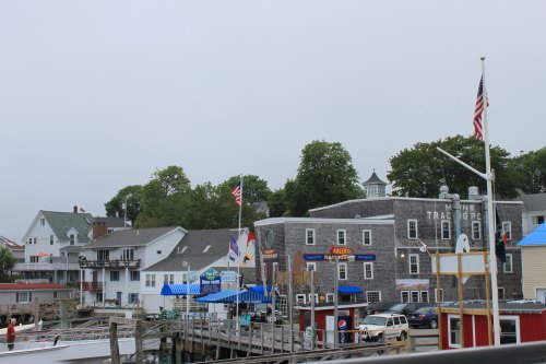 A foggy harbor scene with boats, colorful buildings, and flags in a coastal town.