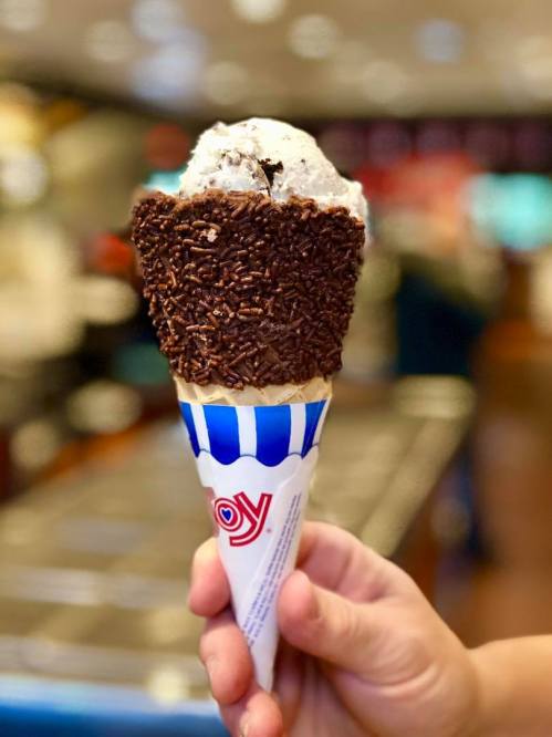 A hand holds an ice cream cone with chocolate sprinkles and a scoop of cookies and cream ice cream on top.