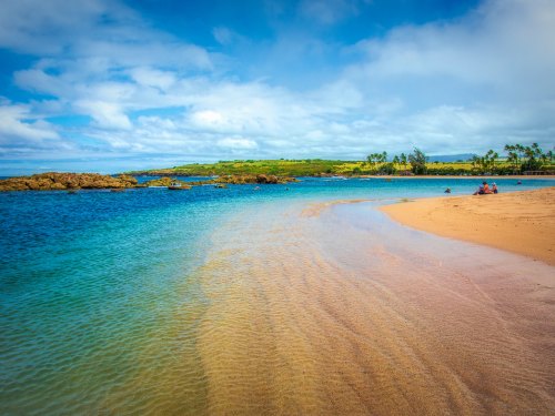 A serene beach scene with clear blue water, gentle waves, and a sandy shore under a bright sky.
