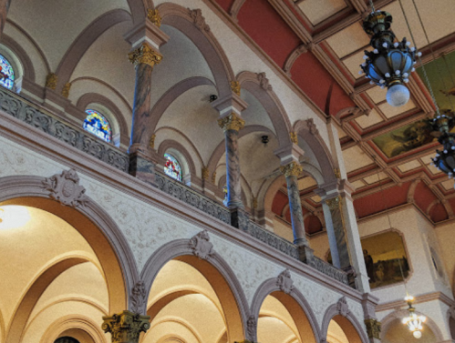 Interior of a grand building featuring arched columns, stained glass windows, and ornate ceiling details.