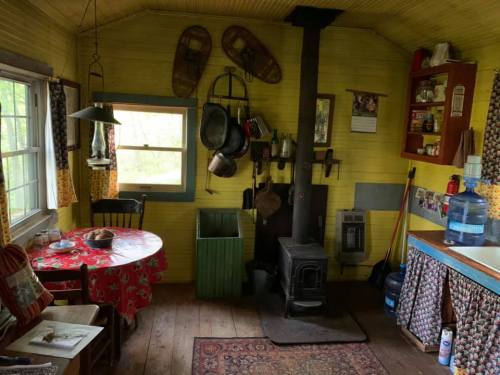 Cozy kitchen with yellow walls, a round table, wood stove, and rustic decor, featuring snowshoes and vintage kitchenware.