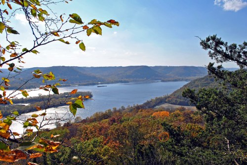 A scenic view of a river winding through colorful autumn foliage and rolling hills under a clear blue sky.